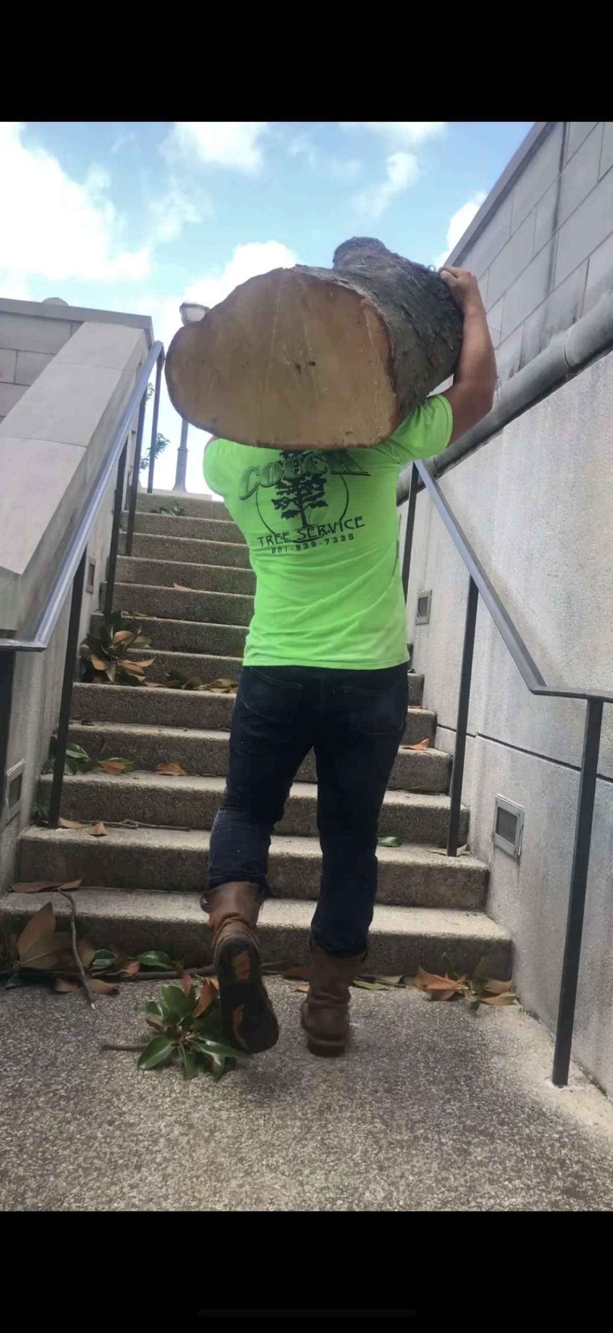 Worker carrying large tree log section down stairs during debris removal