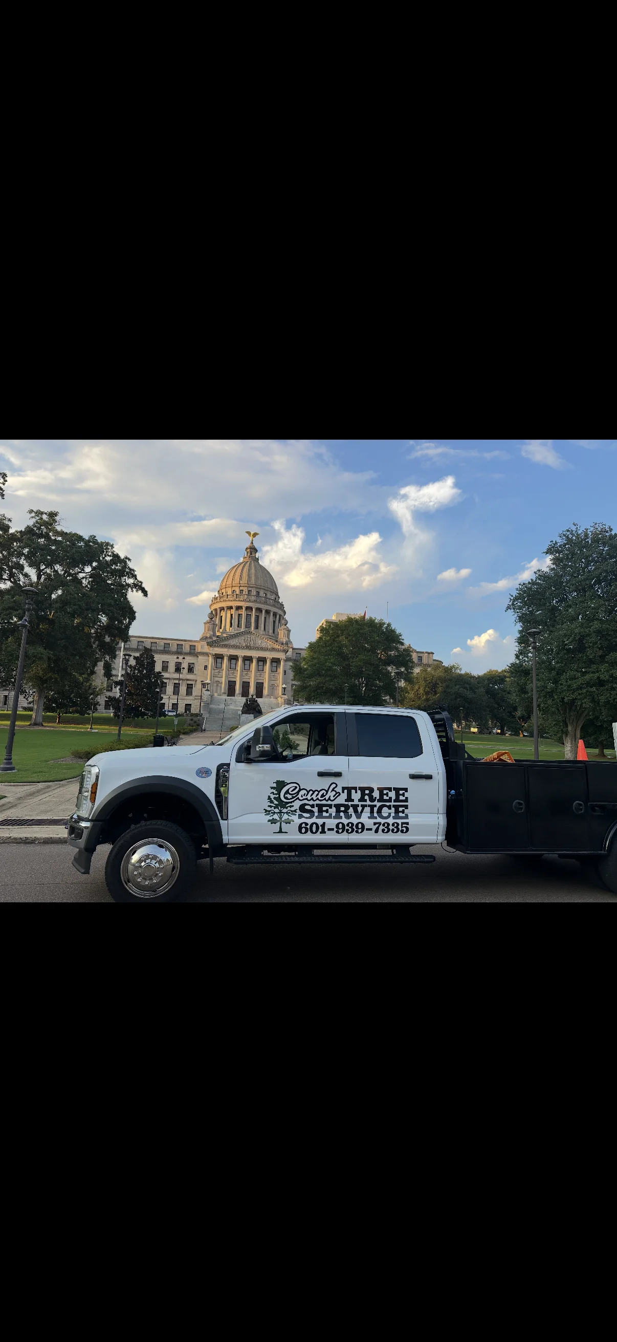White tree service truck with equipment parked at state capitol grounds with mature trees